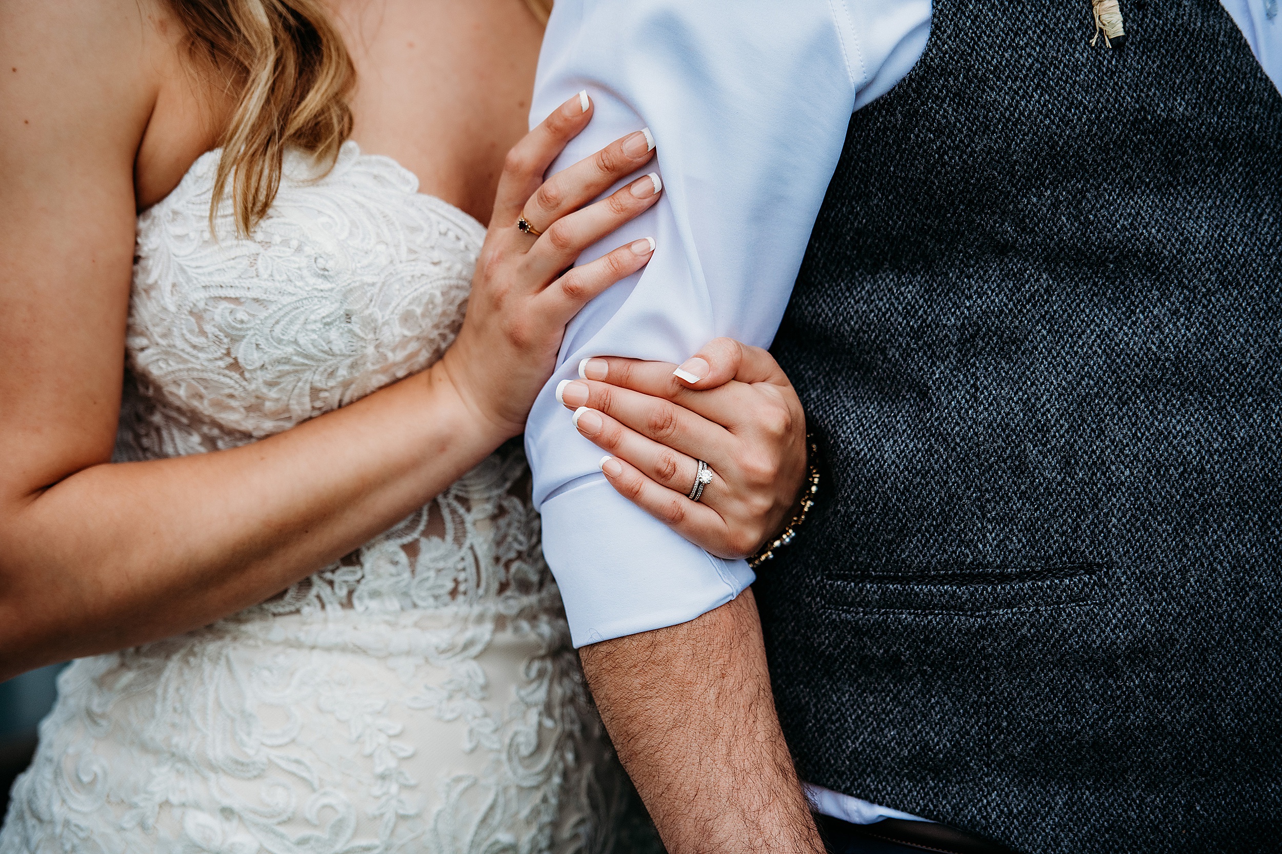close up of a bride holding a grooms arm with her wedding ring on display
