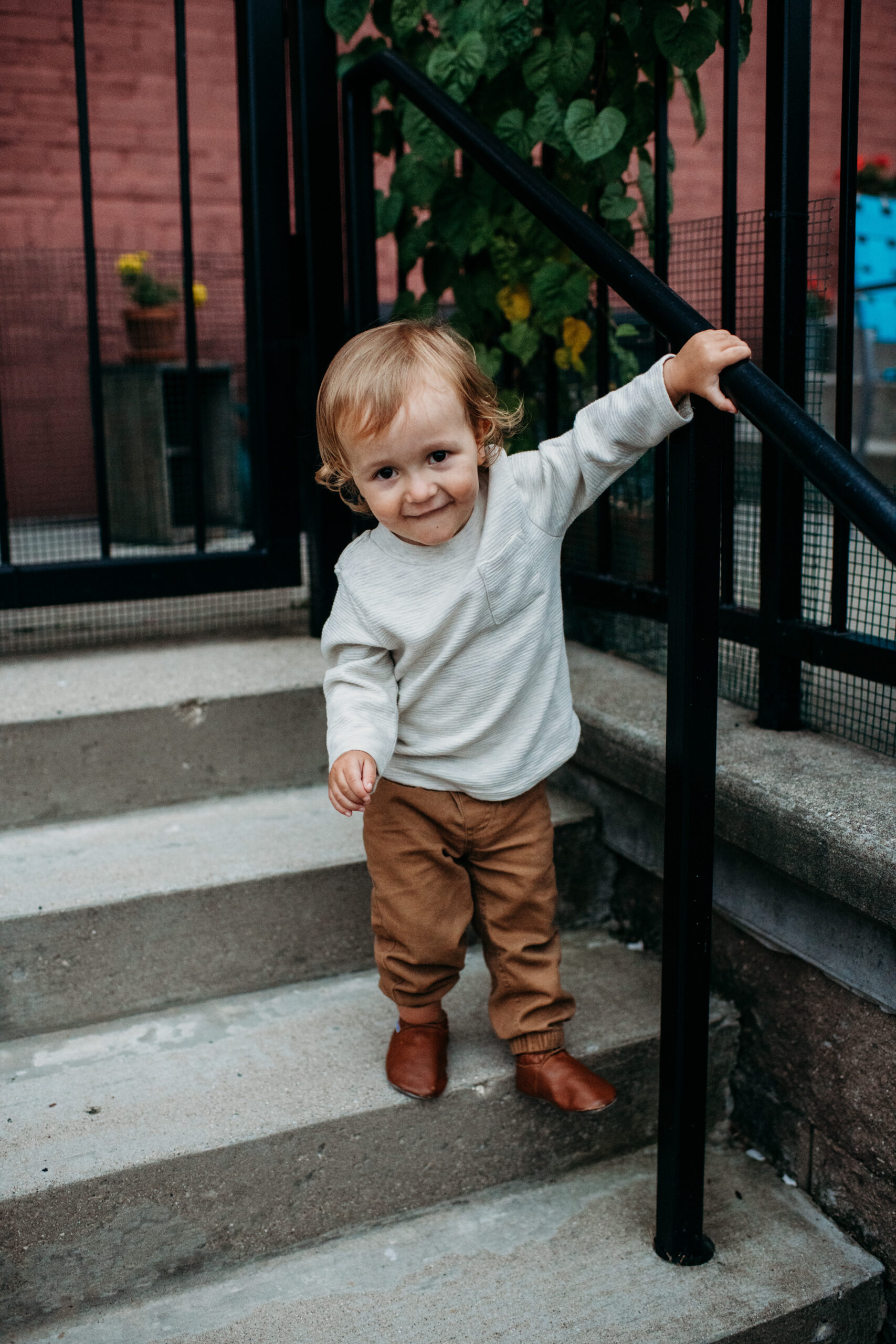 little boy in white shirt and brown pants playing on stairs