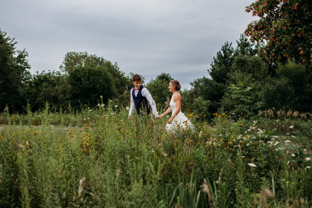bride and groom holding hands and walking through a wildflower field