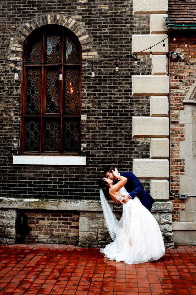 bride and groom sharing a dipping kiss outside a brick building