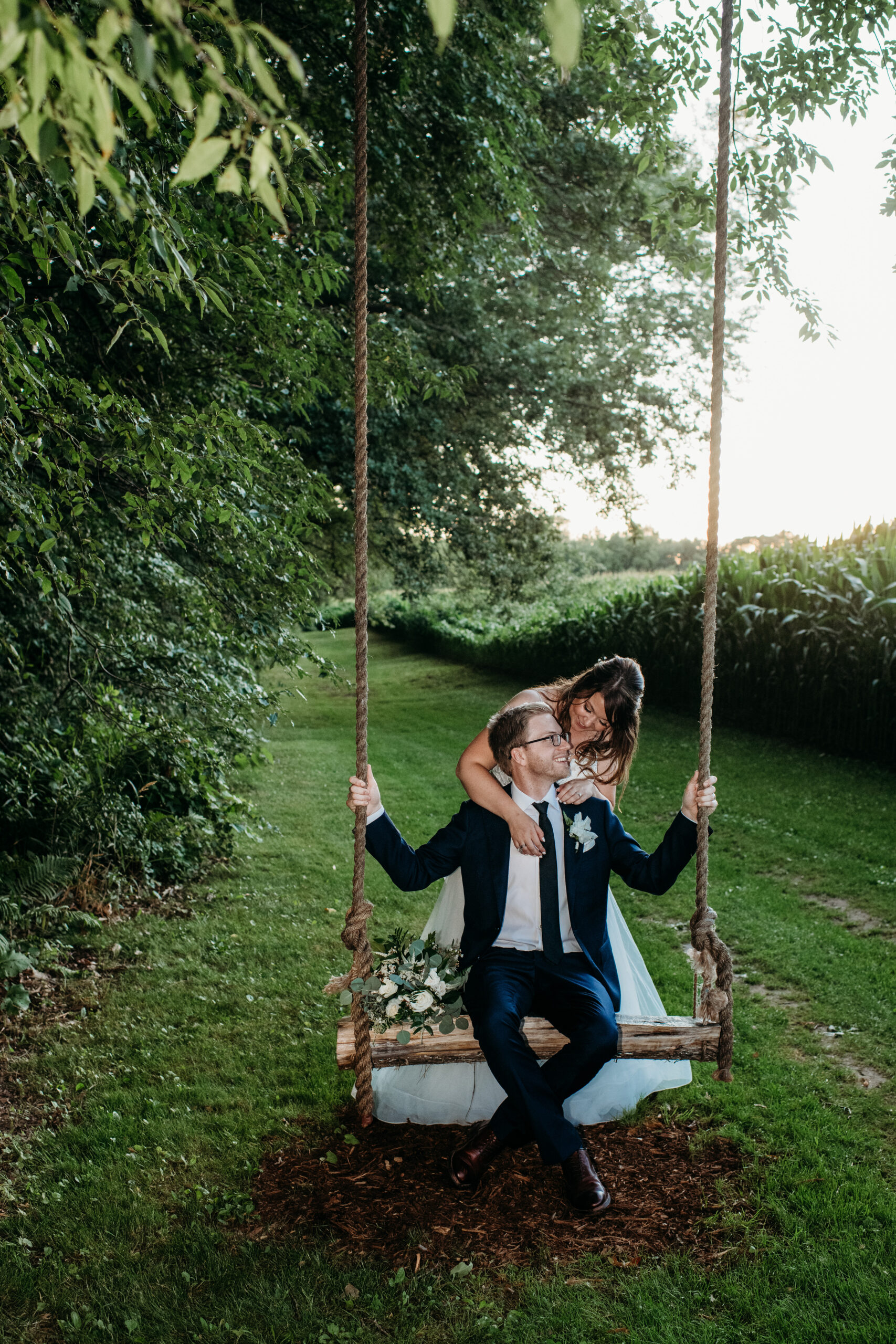 groom sitting on a swing with his bride hugging him Wisconsin outdoor wedding venues